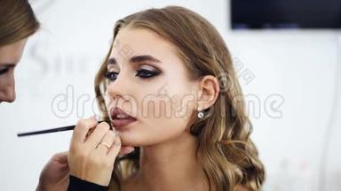 美容店年轻美丽时尚模特.. 化妆师用一支黑色的刷子涂在嘴唇上